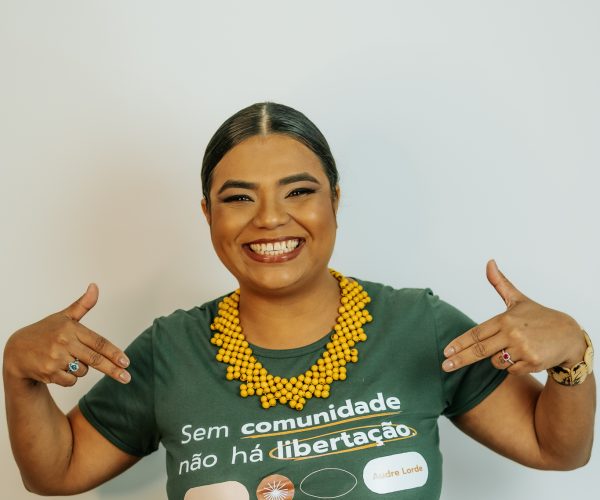 Mulher negra feliz com os dedos apontados para a frase da sua camisa