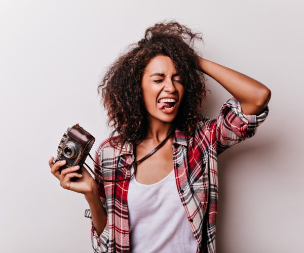 Mulher sorridente segurando uma câmera fotográfica vintage, representando atividades para substituir o celular com hobbies criativos e descontraídos.
